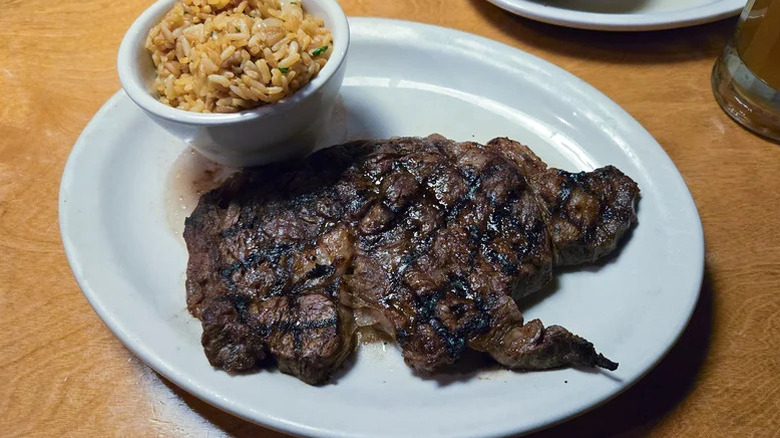 The Fort Worth ribeye from Texas Roadhouse on a white place with a side of rice