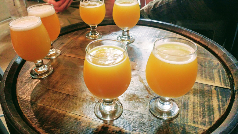 Six glasses of hazy east coast IPA beer sit on a barrel top.