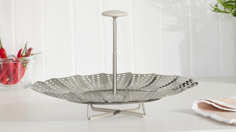 Expanding stainless steel steamer on white countertop near a bowl of chiles and a cloth napkin