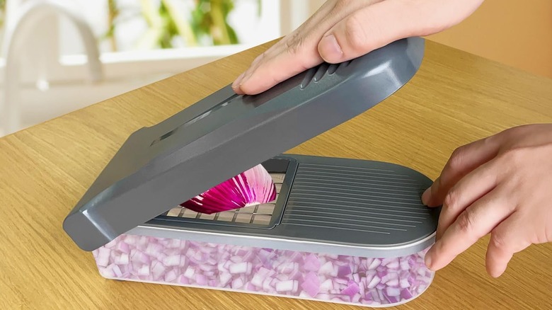 Person's hands using gray and translucent vegetable chopper to chop a red onion