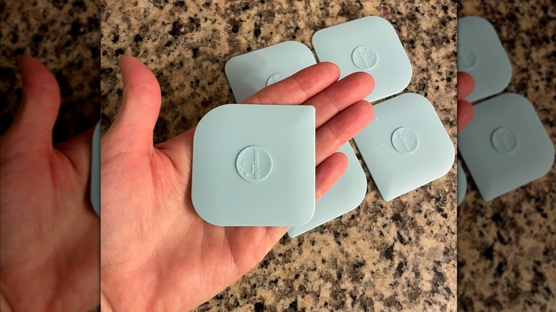 Person's hand holding a light blue silicone pan scraper with four others in the background on a granite countertop