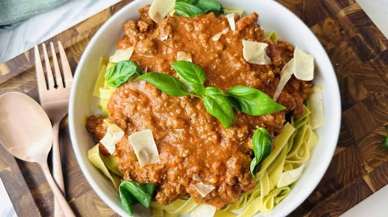 Simple weeknight bolognese with fresh basil on top, served in a white bowl