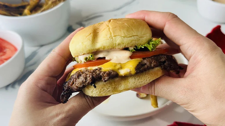 Classic smash burger with all the fixings being held, ready to eat