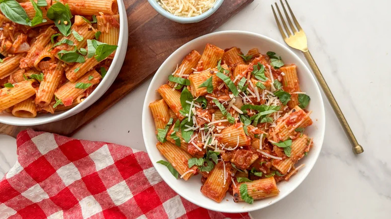 Spicy rigatoni pasta served in a white bowl with herbs and parmesan on top