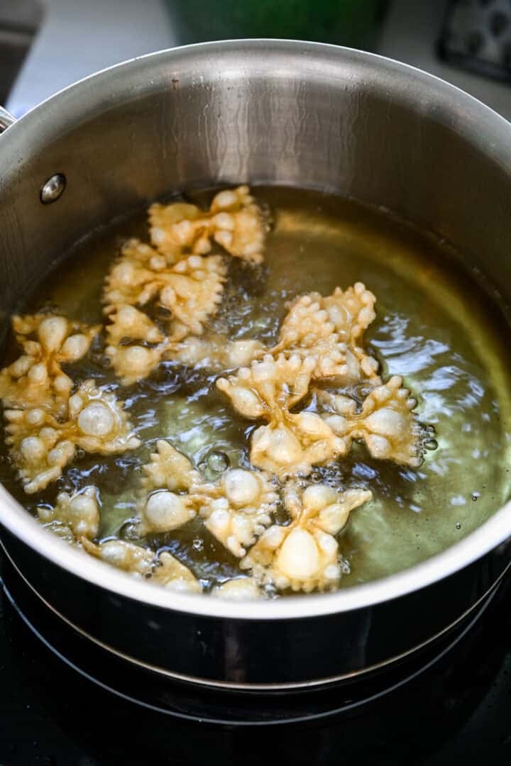 Close up view of bow tie pasta puffing in hot oil in a saucepan.