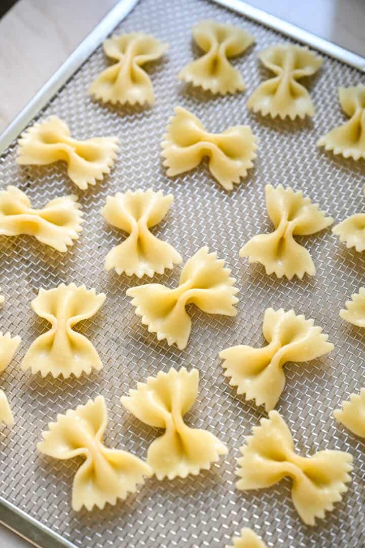 45 degree view of cooked bow tie pasta spread out on a mesh dehydrator tray.