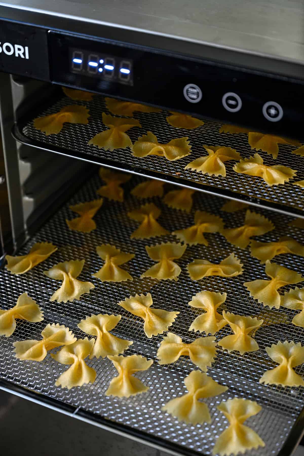Front view of two dehydrator trays of bow tie pasta drying in the machine.