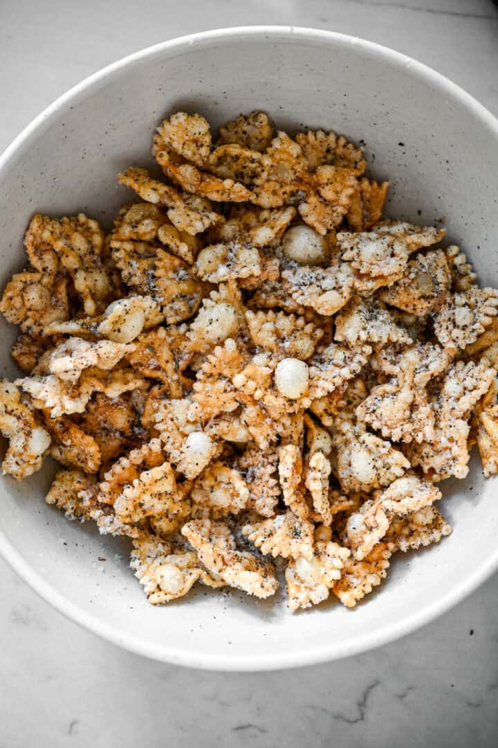 Overhead view of puffed pasta tossed with grated parmesan and black pepper in a white bowl.
