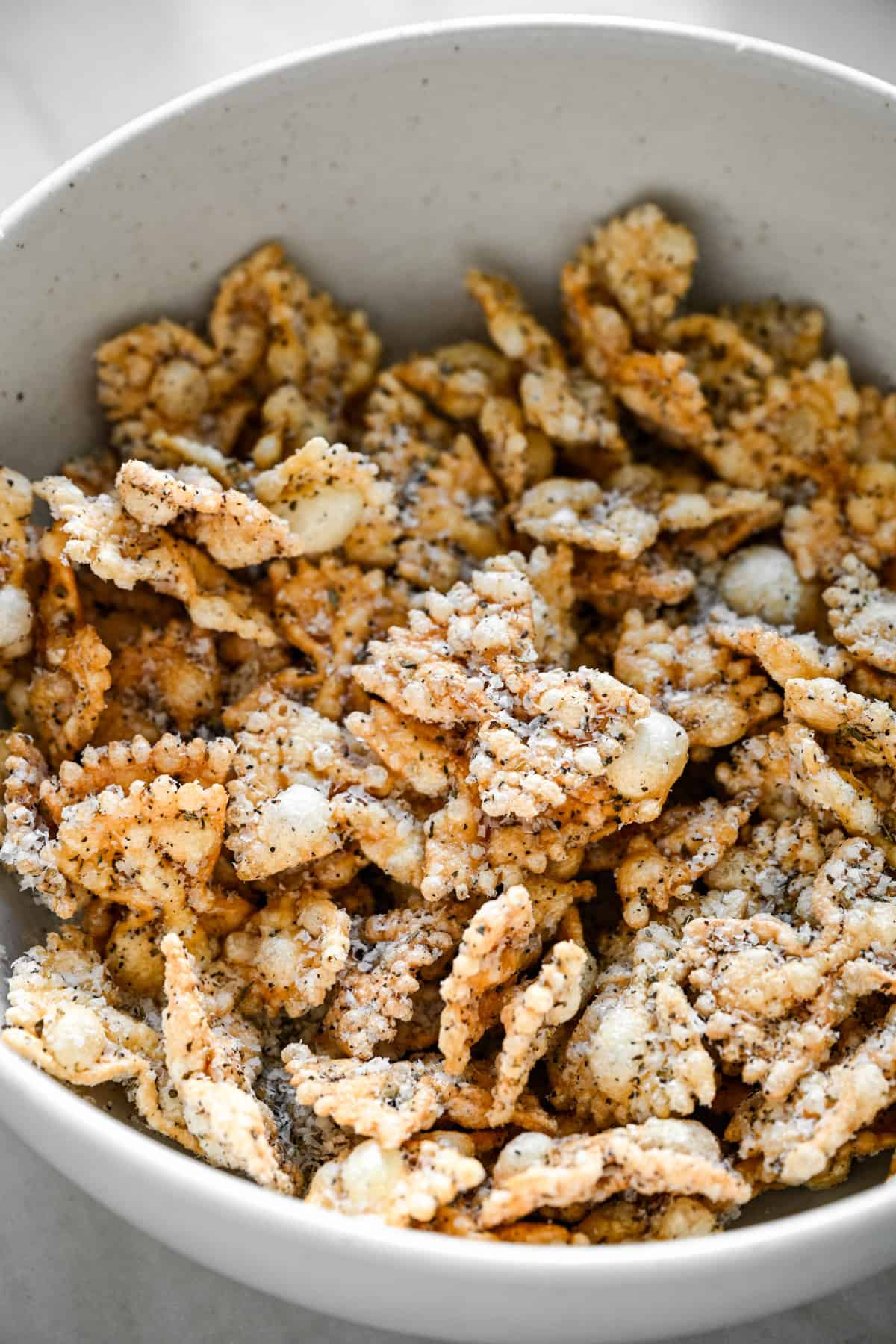 45 degree view of seasoned puffed pasta filling a white speckled bowl.