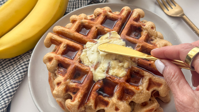 hand spreading butter on syrupy waffle