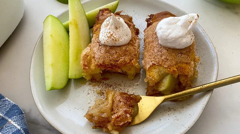White plate with two apple dumplings topped with whipped cream