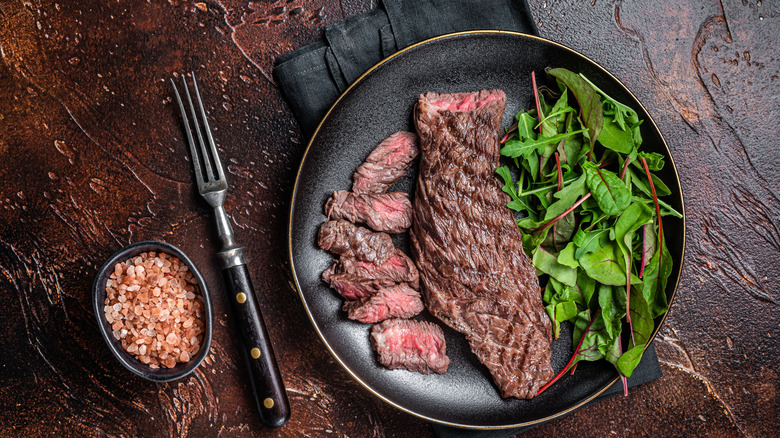 Marinated flank steak on a black plate with salad.