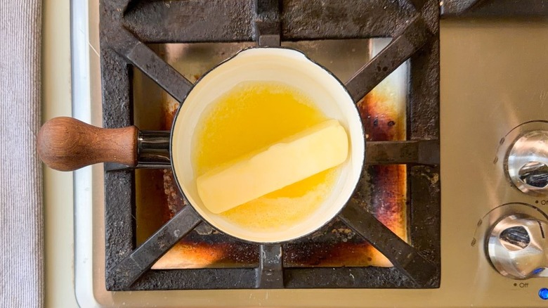 Stick of butter melting in small black saucepan on stovetop