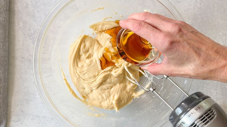 Adding maple syrup to blueberry crumb cake batter in glass bowl