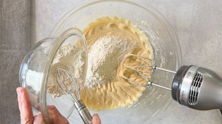 Adding dry ingredients to blueberry crumb cake batter in glass bowl