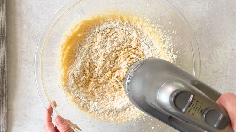 Mixing dry ingredients into blueberry crumb cake batter in glass bowl with hand mixer