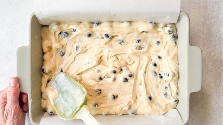 Spreading blueberry crumb cake batter into parchment-lined baking pan with rubber spatula