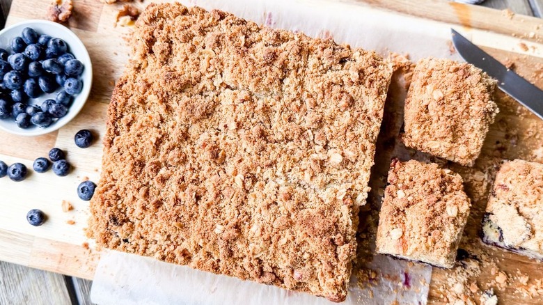 Sliced old-fashioned blueberry crumb cake on cutting board with fresh blueberries