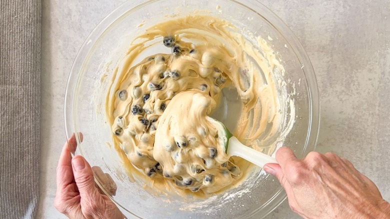 Folding fresh blueberries into blueberry crumb cake batter using rubber spatula in glass bowl