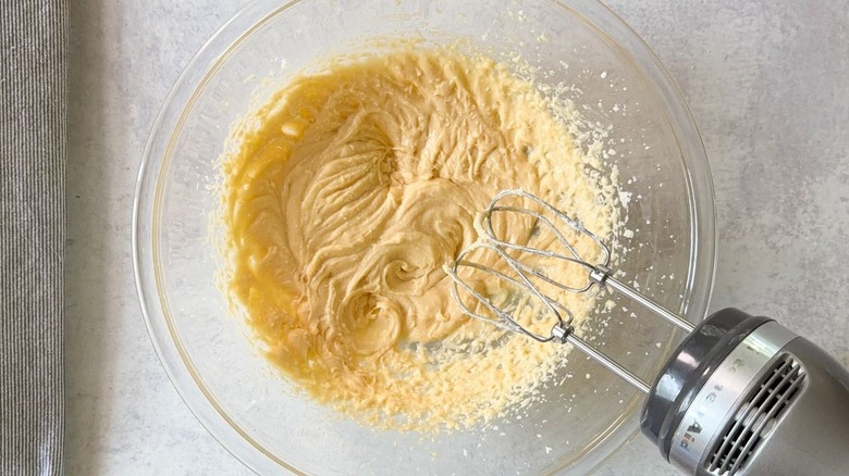 Creamed butter and sugar with egg and vanilla extract in glass bowl with hand mixer