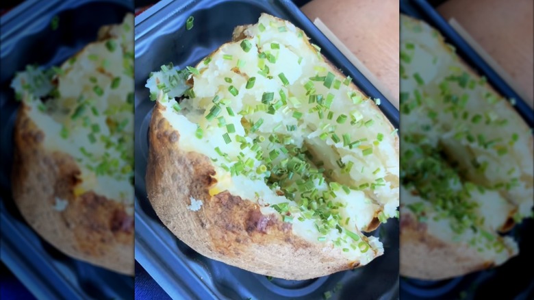 Chive topped Wendy's baked potato in black plastic to-go container.