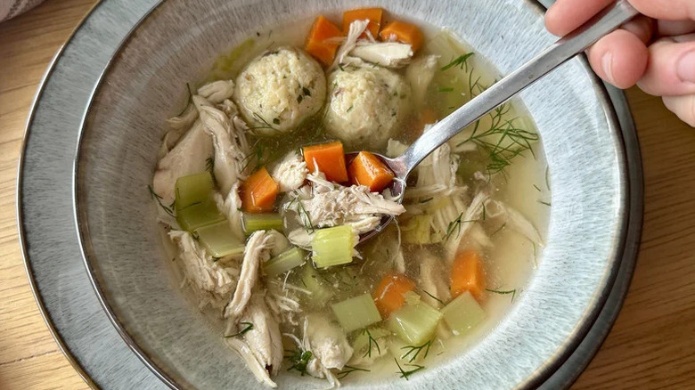 Hand spooning a bite of Classic Comforting Matzo Ball Soup from a bowl