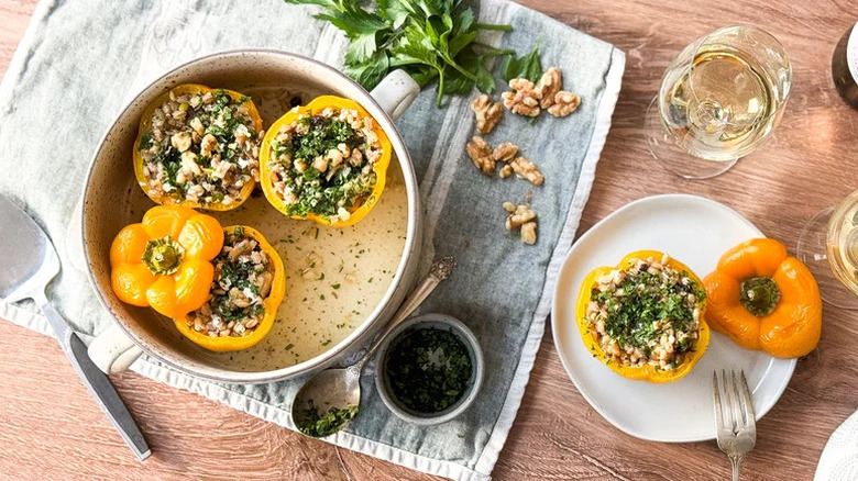 A dish and plate of Barley And Walnut-Stuffed Bell Peppers with glasses of white wine