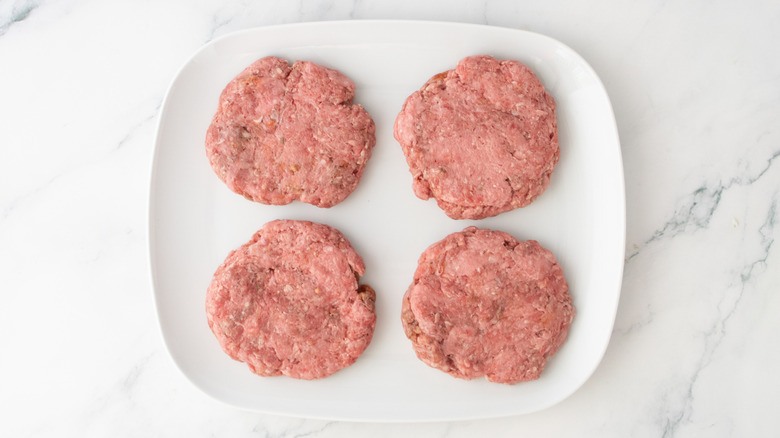 A white plate topped with four burger patties