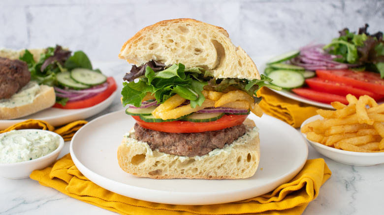 Side shot of a well-stacked gyro burger with toppings and condiments on the side