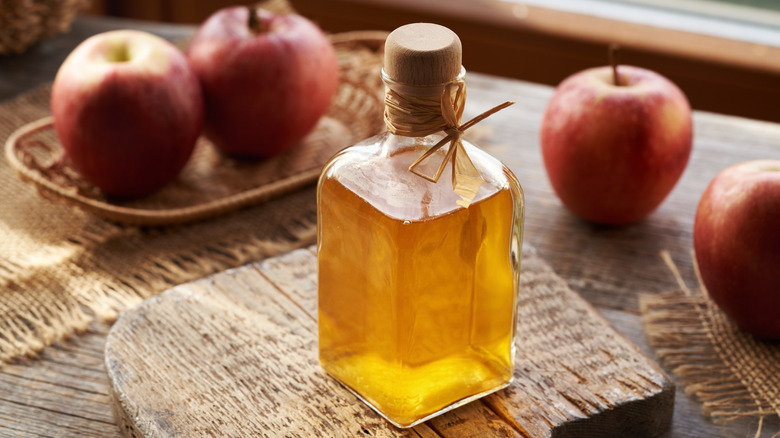 glass bottle of apple cider vinegar on a table surrounded by apples