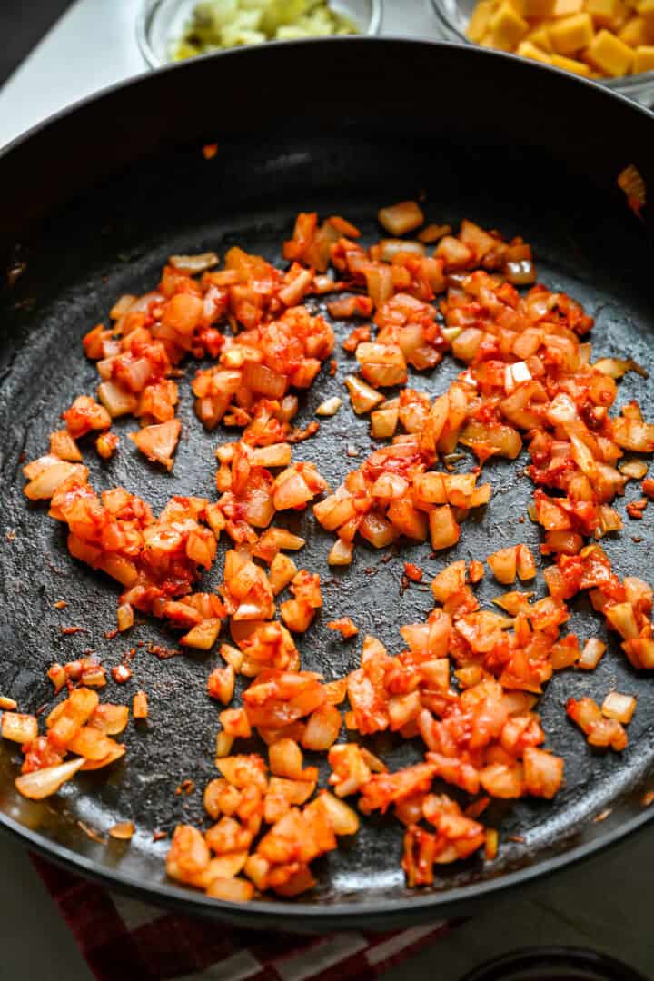 45 degree view of diced onion, garlic and tomato paste cooking in a cast iron skillet