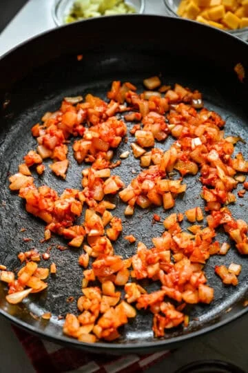 45 degree view of diced onion, garlic and tomato paste cooking in a cast iron skillet