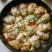 Overhead view of bacon cheeseburger stuffed onions in a Staub cast iron skillet topped with Thousand Island dressing, parsley and sesame seeds, with a jar of dressing and a bowl of sesame seeds beside it