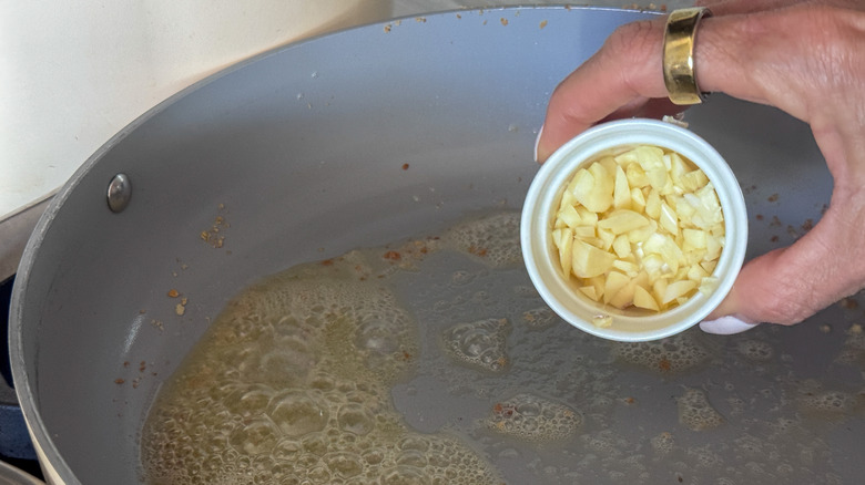 hand adding garlic to pan