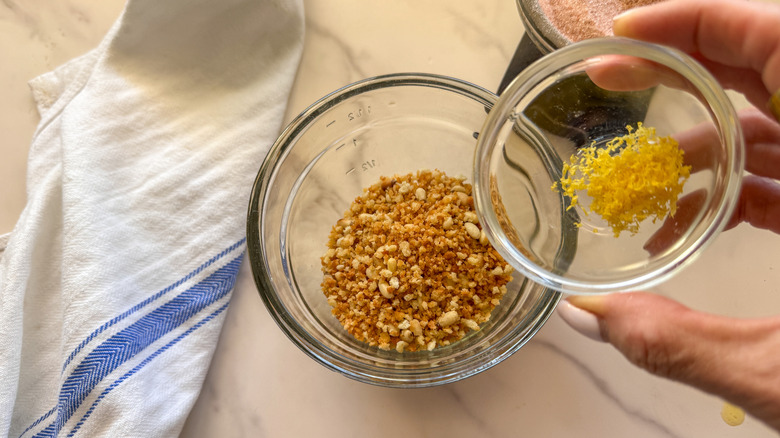 Hand adding small bowl of lemon zest to breadcrumb topping