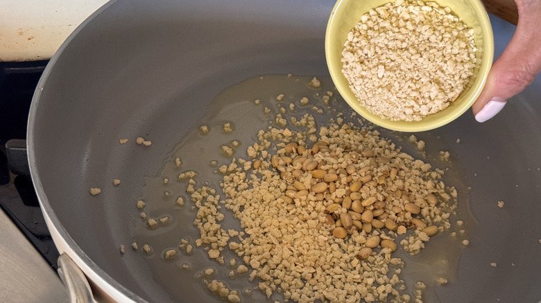 hand adding panko to pan with pine nuts