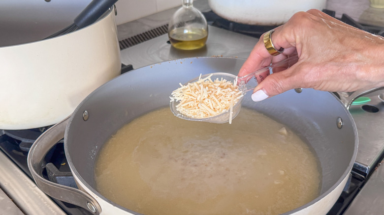Hand holding small scoopful of parmesan over pan with creamy sauce