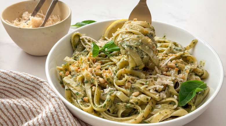 Pesto fettuccine swirled on fork over large bowl of pasta