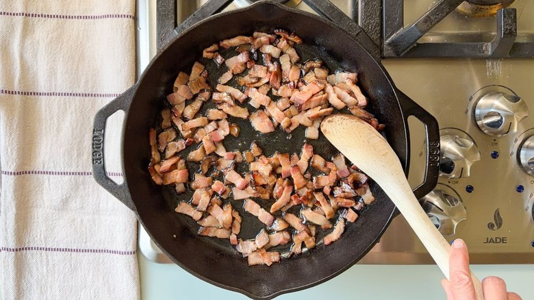 Bacon lardons cooking in cast iron skillet on stovetop