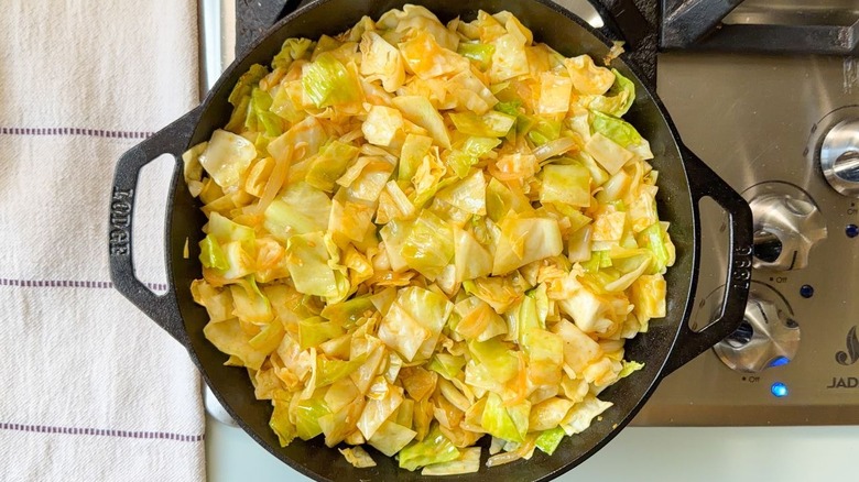 Using tongs to stir cooked cabbage in skillet on stovetop