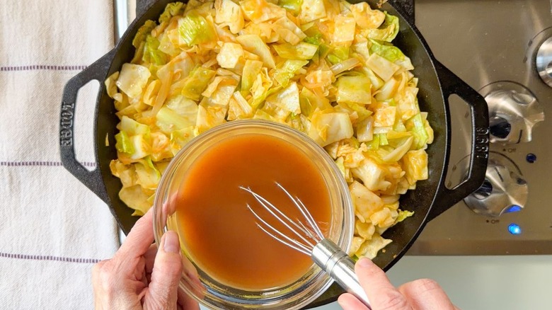 Whisking sauce for cowboy cabbage in a small glass bowl over skillet on stovetop
