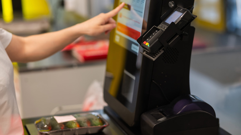 A person interacting with a self-checkout kiosk to purchase cucumbers