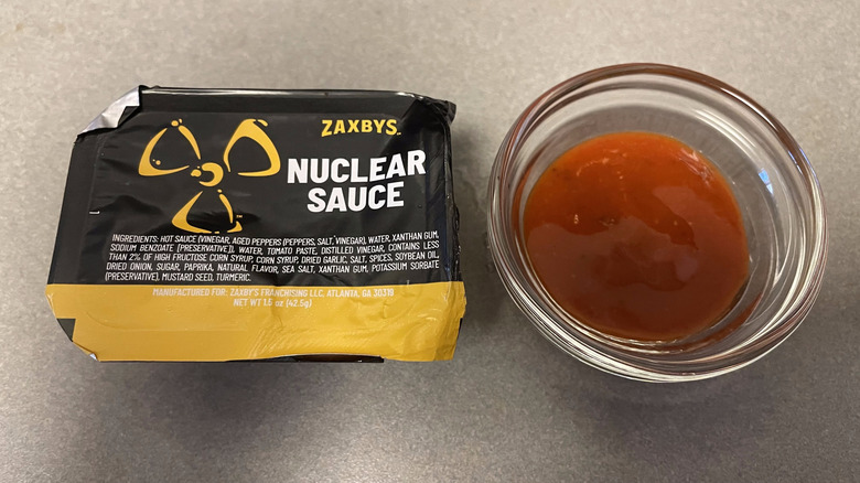 A packet of Nuclear Sauce sits on a gray counter next to a dish of dark orange sauce.