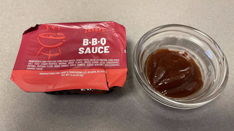 A packet of BBQ Sauce sits on a gray counter next to a dish of brown sauce.
