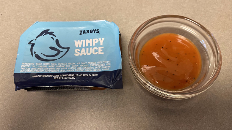 A packet of Wimpy Sauce sits on a grey counter next to a dish of orange sauce.