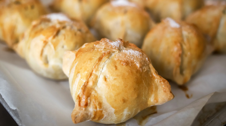 Several apple dumplings wrapped in pastry on a baking sheet.