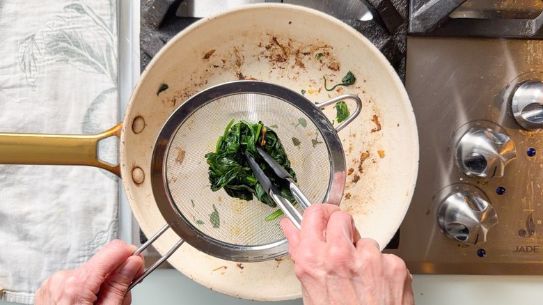 Pressing wilted spinach in fine mesh sieve to remove excess moisture