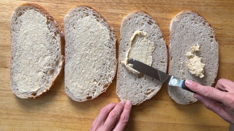 Spreading mayo butter mix on slices of sourdough bread on cutting board
