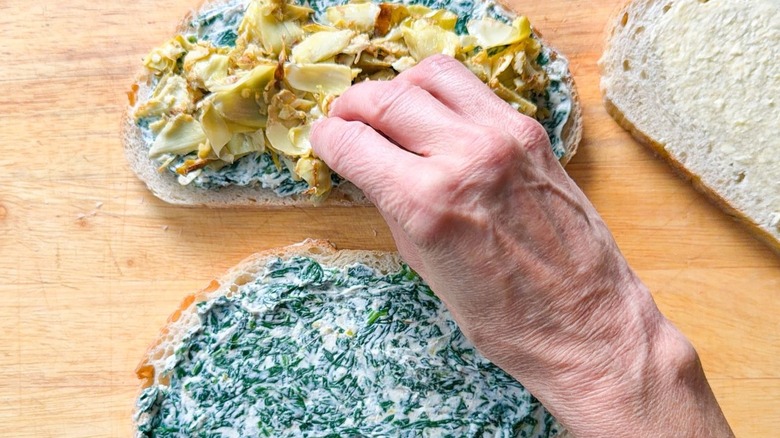 Placing crispy artichoke heart quarters on top of spinach ricotta spread on bread